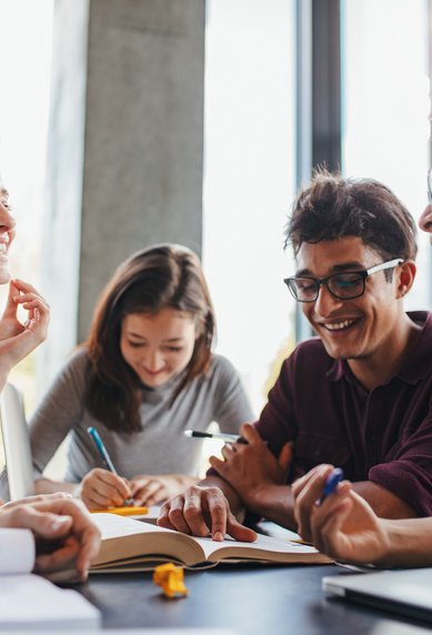 Studierende lachen gemeinsam während einer Gruppenarbeit am Tisch.